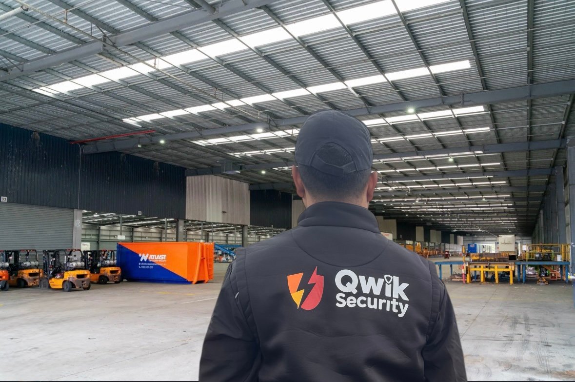 Qwik Security static guard inside a warehouse with forklifts and industrial equipment visible
